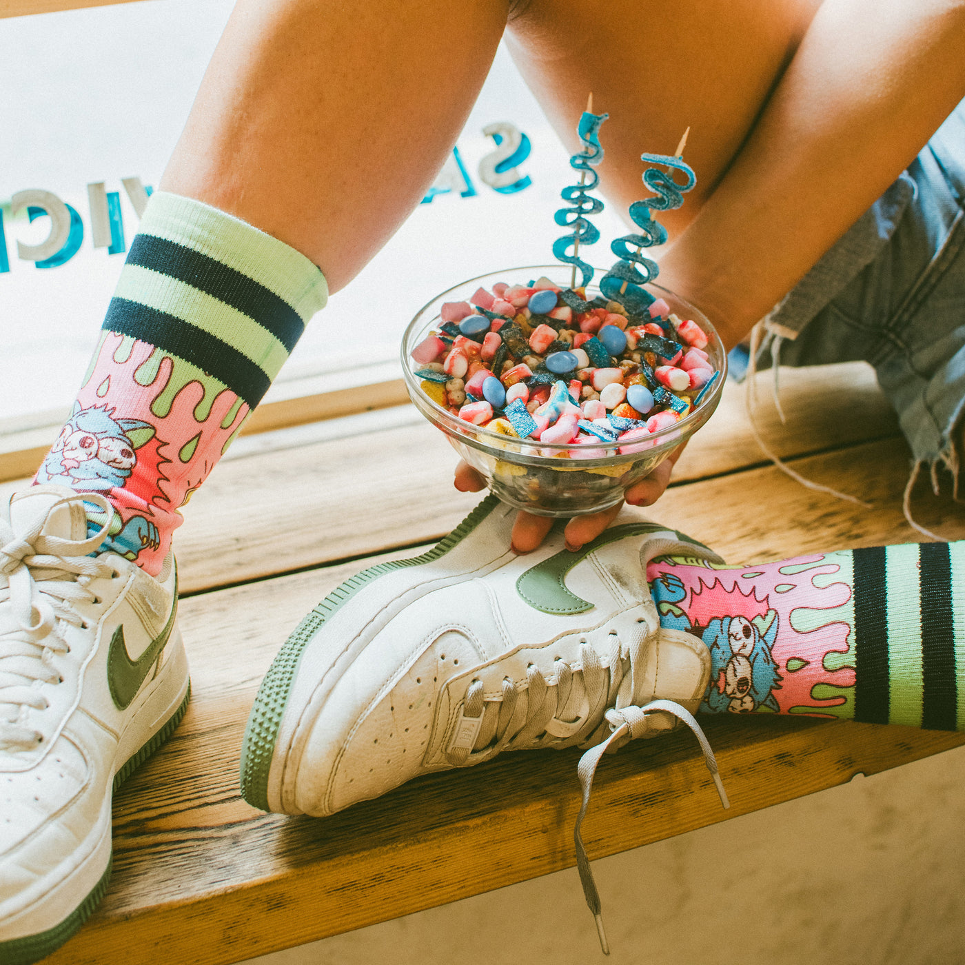 Hand holding bowl of candy resting on legs with funky psychedelic cat socks on american socks